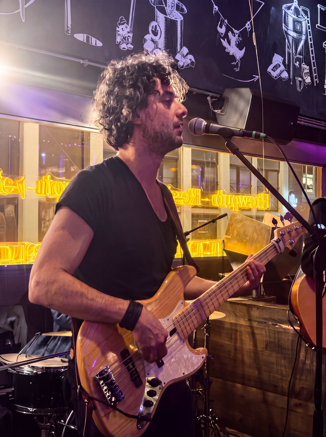 Osman Meyredi singing at the microphone with his bass guitar, warm neon light