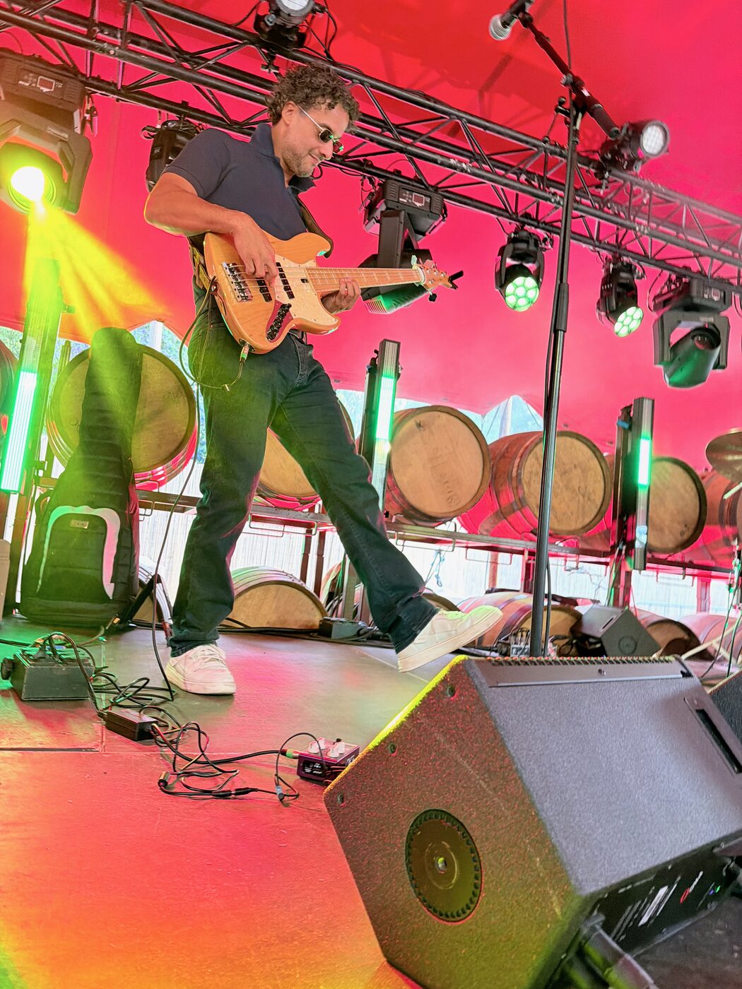 Osman Meyredi playing bass guitar on a festival stage lined with wine barrels