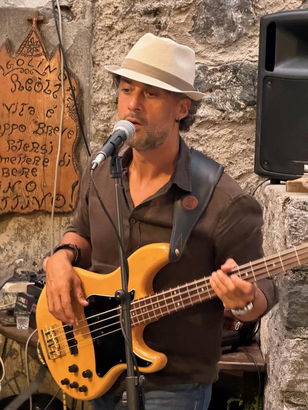 Osman Meyredi in a straw hat singing at the microphone, bass guitar in hand