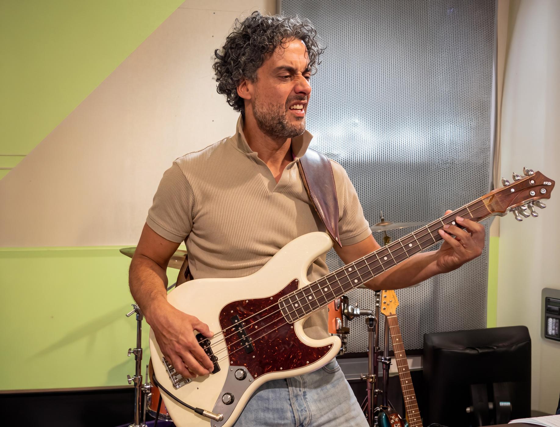 Osman Meyredi playing a white bass guitar, eyes closed