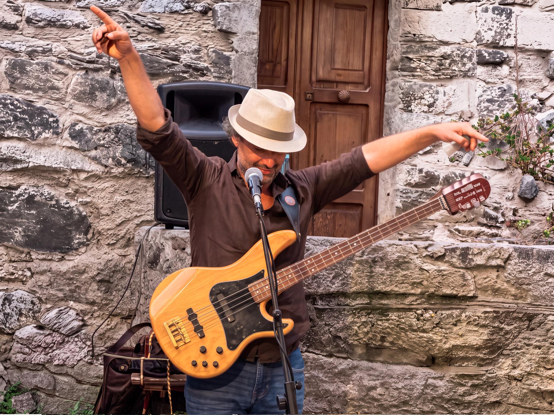 Osman Meyredi in a straw hat, arms outstretched, with his bass guitar at an outdoor show