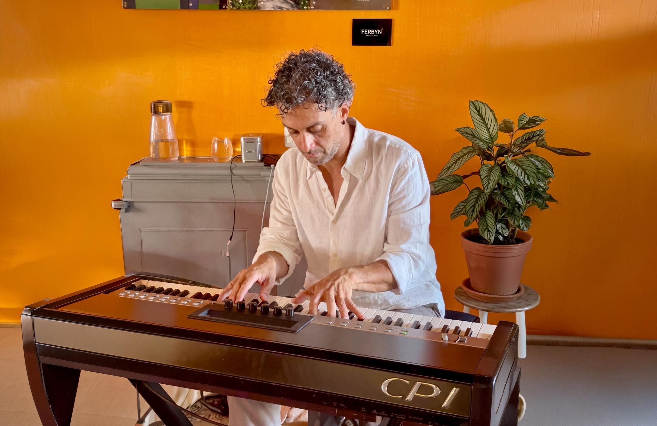 Osman Meyredi playing a stage piano against an orange wall