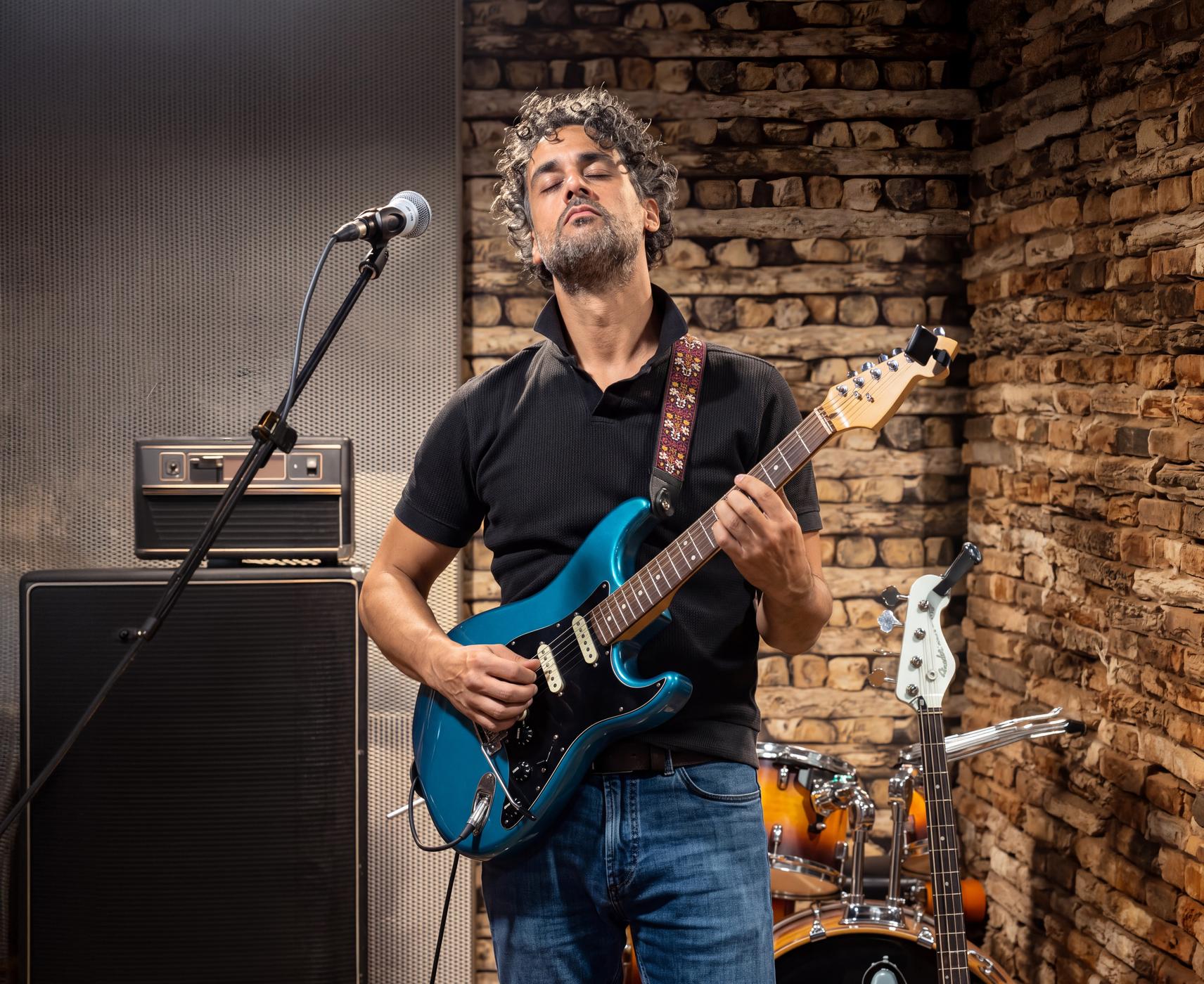 Osman Meyredi playing a blue electric guitar, eyes closed