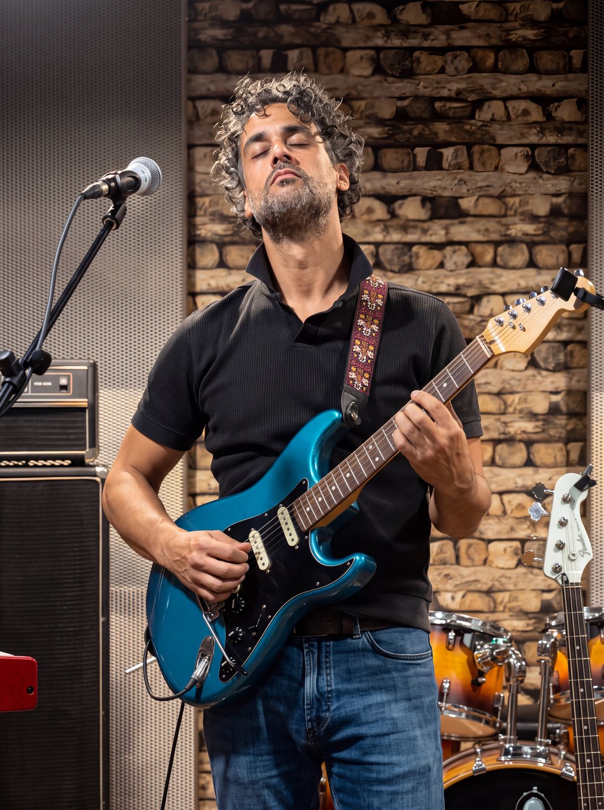 Osman Meyredi playing a blue electric guitar against a brick wall